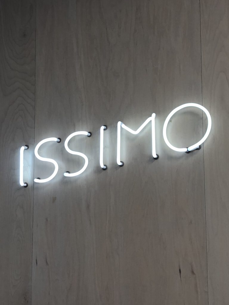 Neon Issimo sign on white wall.